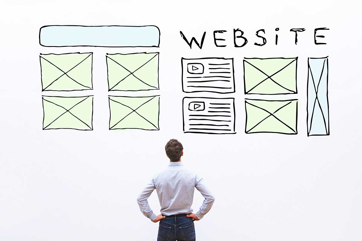 Website Refresh or a Full Redesign erson standing with hands on hips looking at a sketched website wireframe layout on a white background, representing website redesign or site structure planning.